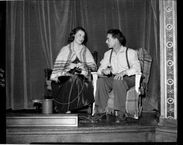 Performance of skit at Edison auditorium. Man and woman in rocking chairs. Woman has a shawl and is knitting
