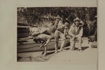 Guy Forcier and Joe Desloge before the start of the motor transit of Grand Canyon. Willie Taylor wets his head at left. The "Esmeralda II" is at the beach