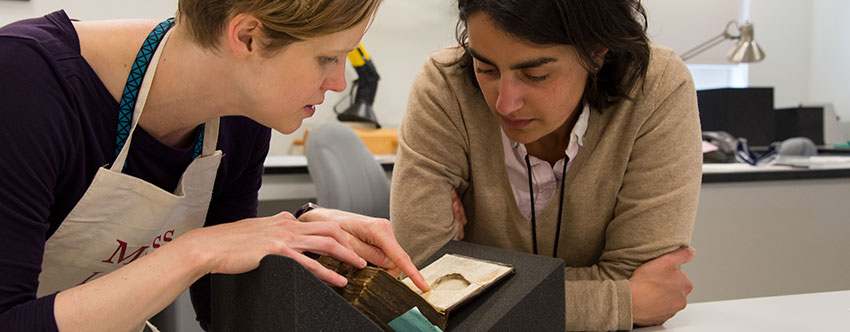 Senior book conservator Andrea Knowlton (left) and Racha Kirakosian, assistant professor of German and the Study of Religion at Harvard University, look at a pear-shaped recess inside the front cover of a 15th-century Dutch codex known as Huntington Manuscript 1048. Photograph by Kate Lain. Senior book conservator Andrea Knowlton (left) and Racha Kirakosian, assistant professor of German and the Study of Religion at Harvard University, look at a pear-shaped recess inside the front cover of a 15th-century Dutch codex known as Huntington Manuscript 1048. Photograph by Kate Lain.